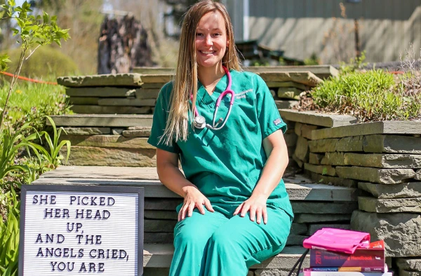 A smiling woman in nurse scrubs sitting on stone steps.